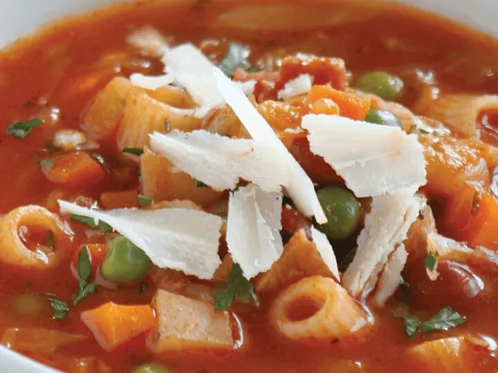 Red pasta soup with carrots, peas, bacon, Parmesan, and herbs.