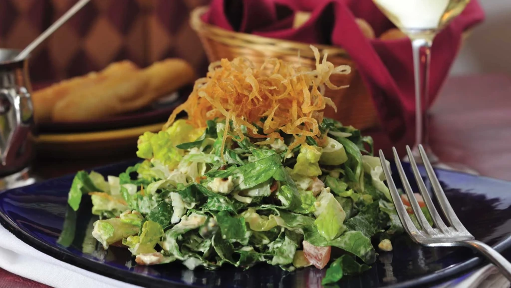 Fresh green salad with creamy dressing and crispy onions on a blue plate.