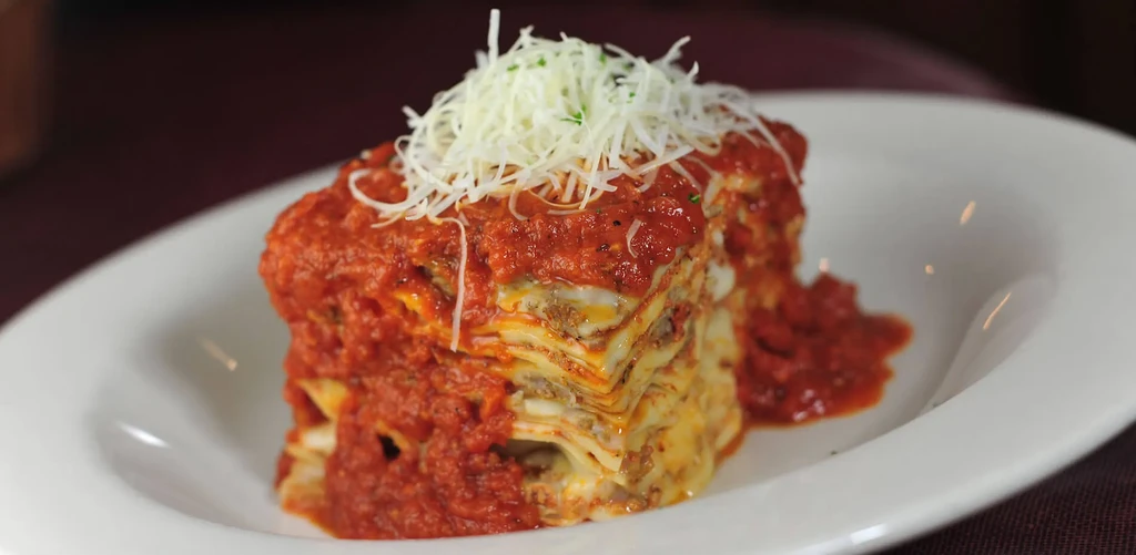 Layered lasagna topped with red sauce, grated cheese, and green herbs.
