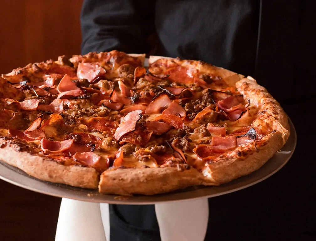 Heavily topped meat pizza with golden crust on metal peel.