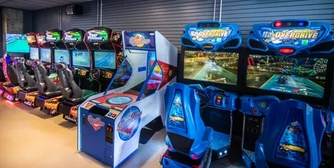 Well-lit arcade machines: racing simulators, H2 OVERDRIVE, and disc-tossing game.