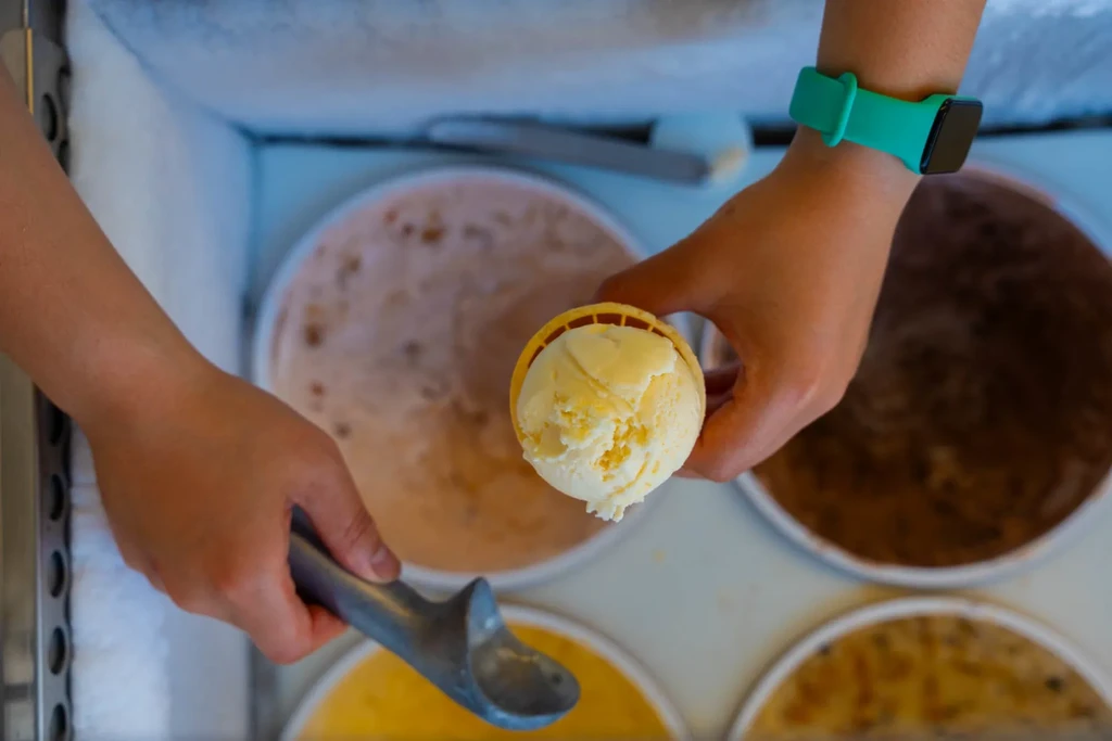 Hands scooping light ice cream into a waffle cone.