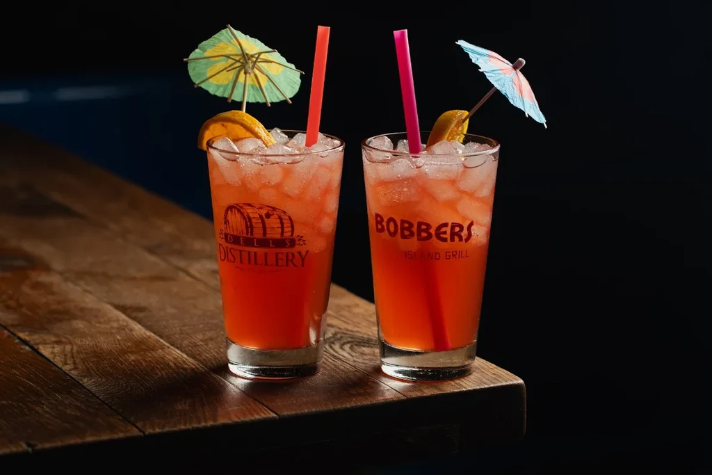 Two iced reddish-orange drinks with citrus, umbrellas, and logos.