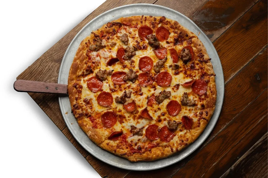 Golden-brown pepperoni and sausage pizza on a silver pan with a peel.