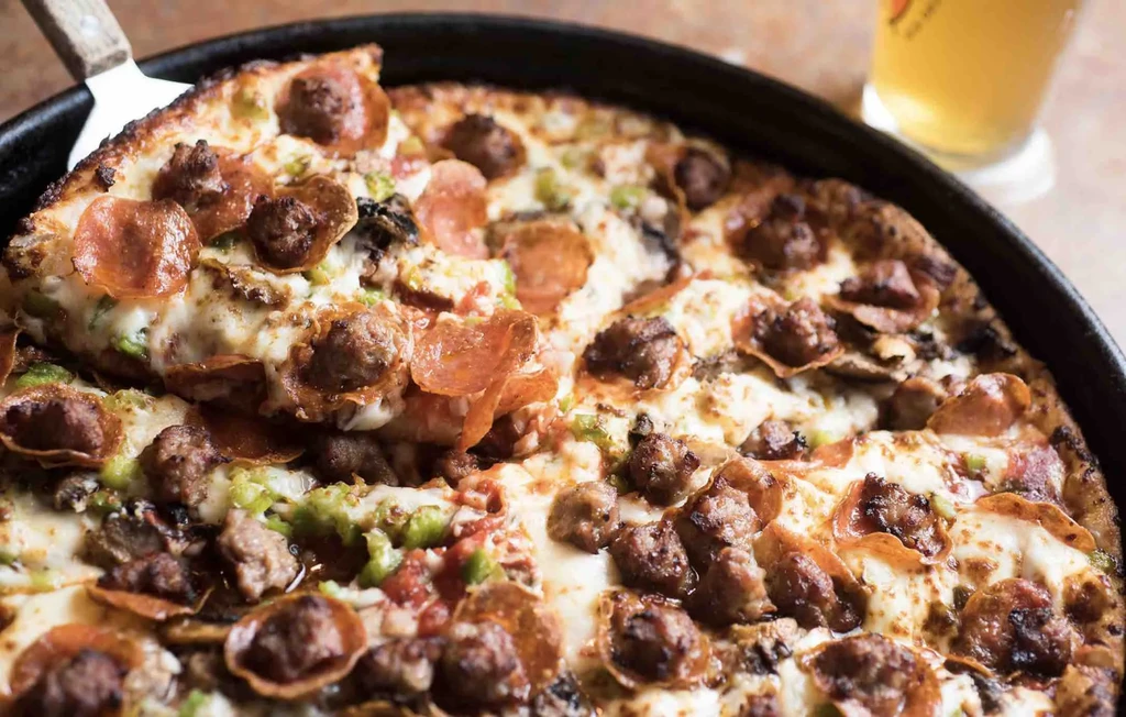 Deep-dish pizza slice with melted cheese and toppings lifted from pan.