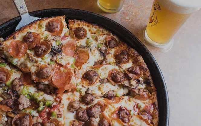 Deep-dish pizza with pepperoni, sausage, vegetables, cheese; server lifting slice.