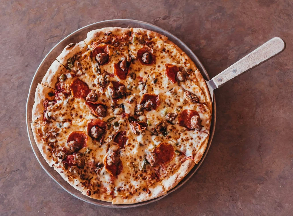 Overhead, freshly baked pizza with pepperoni, sausage, peppers, onions, cheese.
