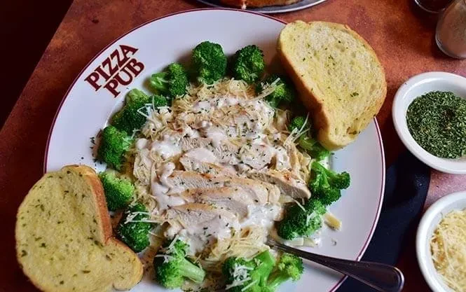 Top-down: Pasta with chicken, broccoli, garlic bread, 'PIZZA PUB' plate.