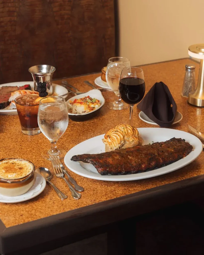 Restaurant table laden with barbecued ribs, gratin, salad, and drinks.
