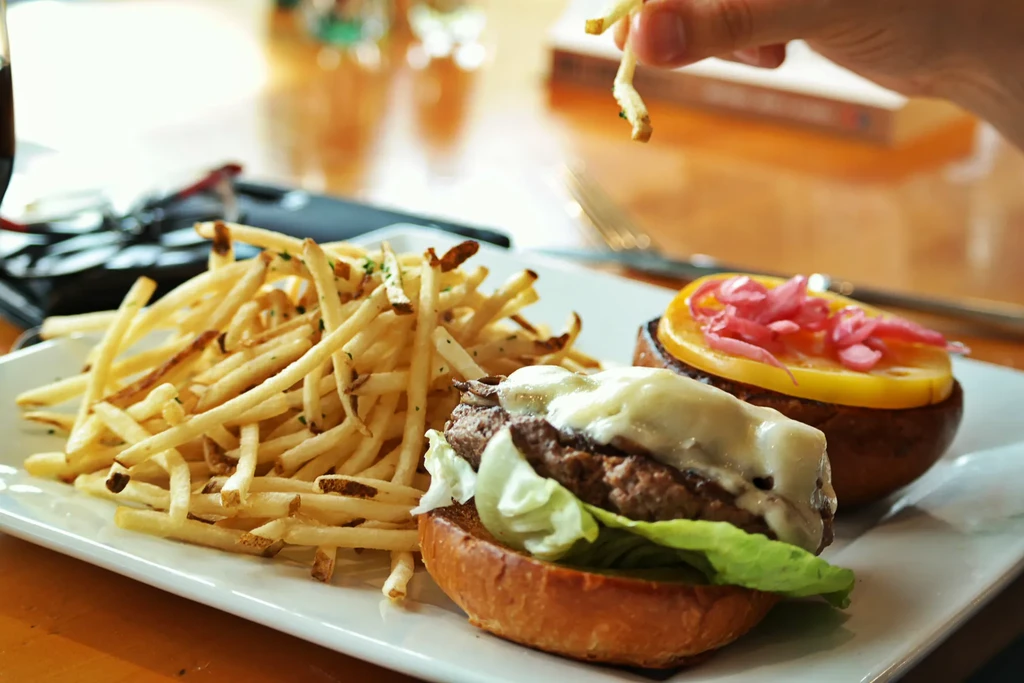 Open-faced gourmet burger, golden fries, and a hand holding a fry.