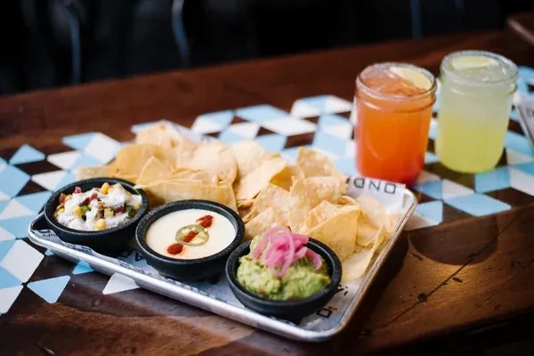 Tortilla chips, queso, guacamole, corn dip, and two lime drinks.