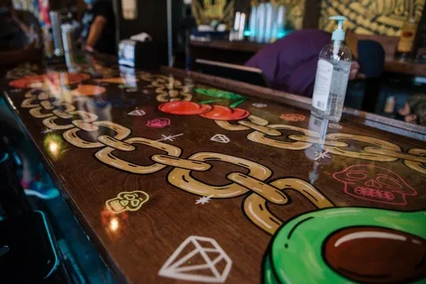 Glossy bar top with cartoon chains, cherries, diamonds, skulls, avocado.