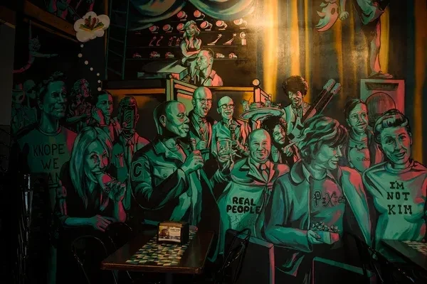 Bold, colorful mural depicting diverse cartoon figures in a retro bar.
