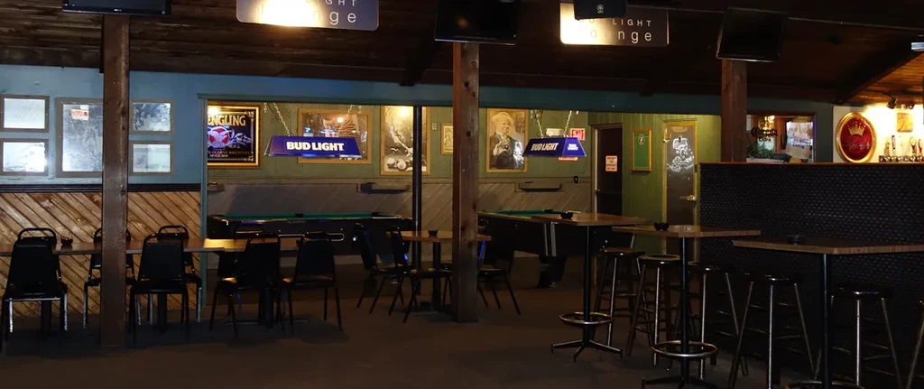 Dimly lit rustic bar interior with pool tables and a bar counter.