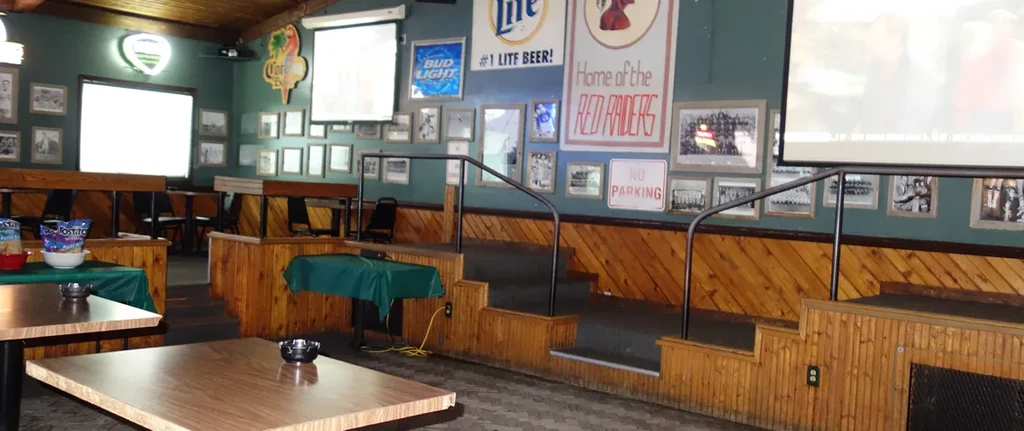 Casual sports bar interior with dark walls, various signs, and projector screens.