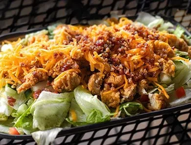 Fried chicken salad with cheddar, bacon, tomato, in a black basket.