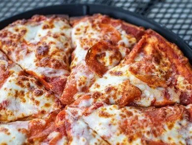 Sliced, hot pepperoni pizza with bubbly melted cheese in a dark pan.