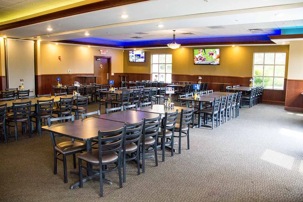 Empty dining hall with tables, chairs, yellow walls, and TVs.