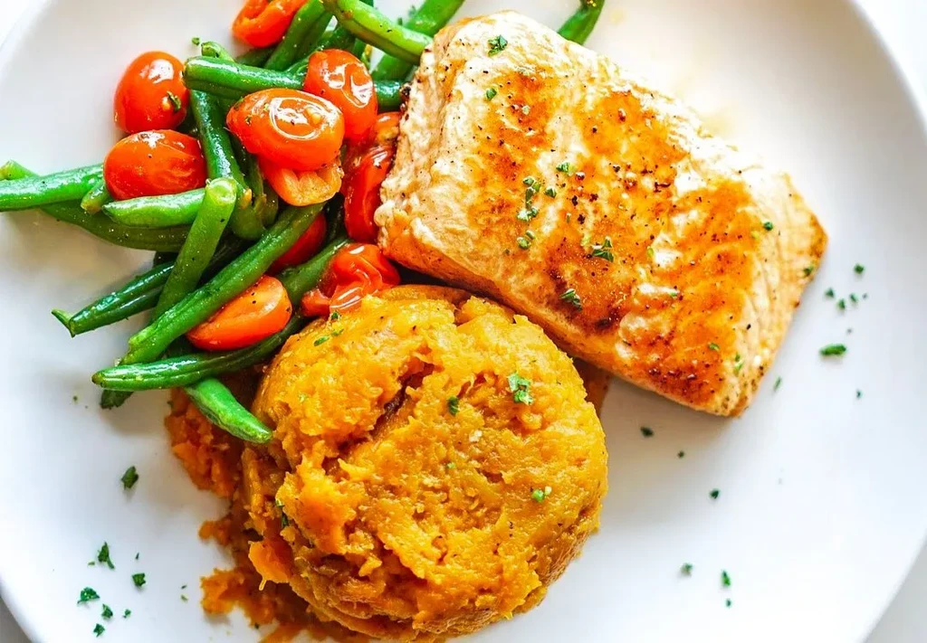 Plated meal with golden fish, green beans, tomatoes, and orange puree.