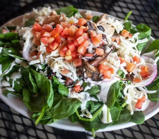 Colorful spinach salad topped with cheese, tomatoes, red onion, and protein.