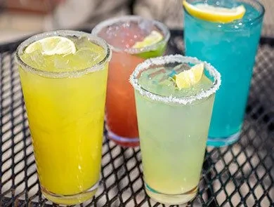 Five colorful garnished cocktails on a black mesh table.