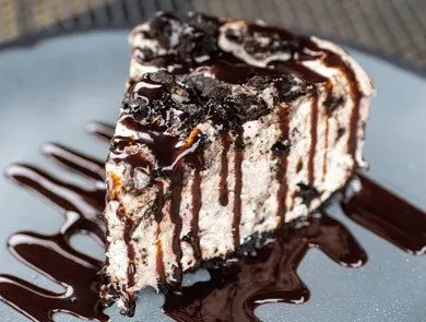 Slice of creamy cookie dessert drenched in chocolate sauce.