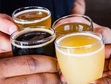 Four flight glasses of different beers held by two people.