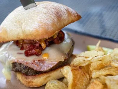 Burger with melted white cheese, crispy bacon, and potato chips.