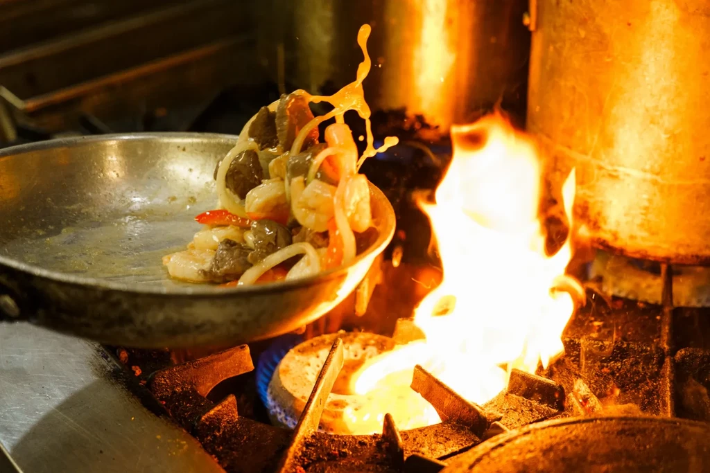 Shrimp and meat stir-frying in a pan over intense orange flames.