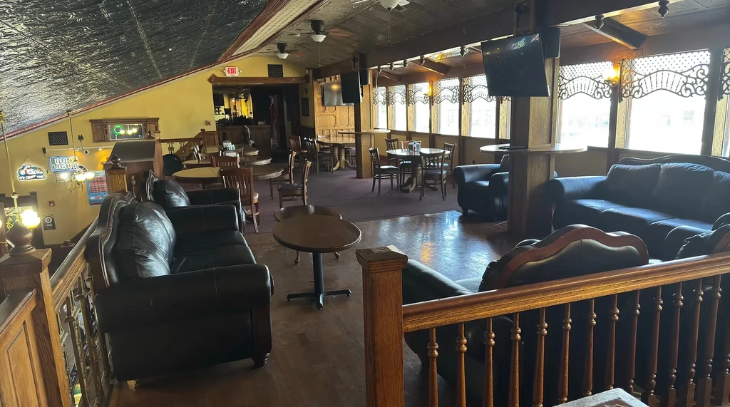 Restaurant mezzanine with dark leather sofas, wooden tables, and bar.
