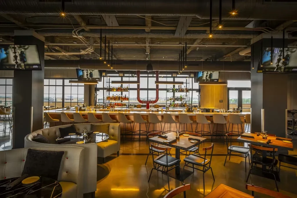 Modern restaurant interior, long bar with unique red U-fixture, various seating.