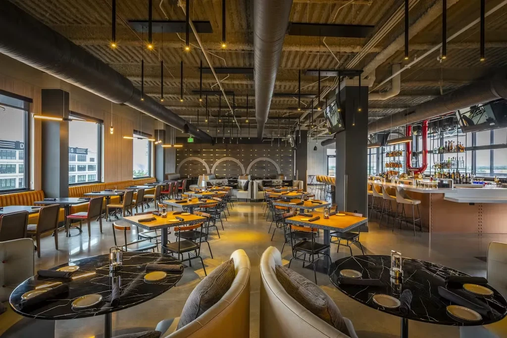 Modern industrial-chic restaurant with diverse seating, bar, and city views.
