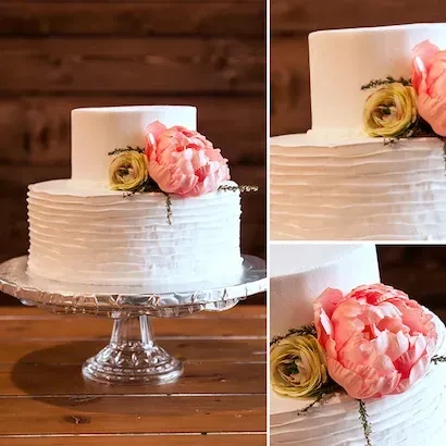 Two-tier white cake, textured frosting, pink flowers, wooden background.