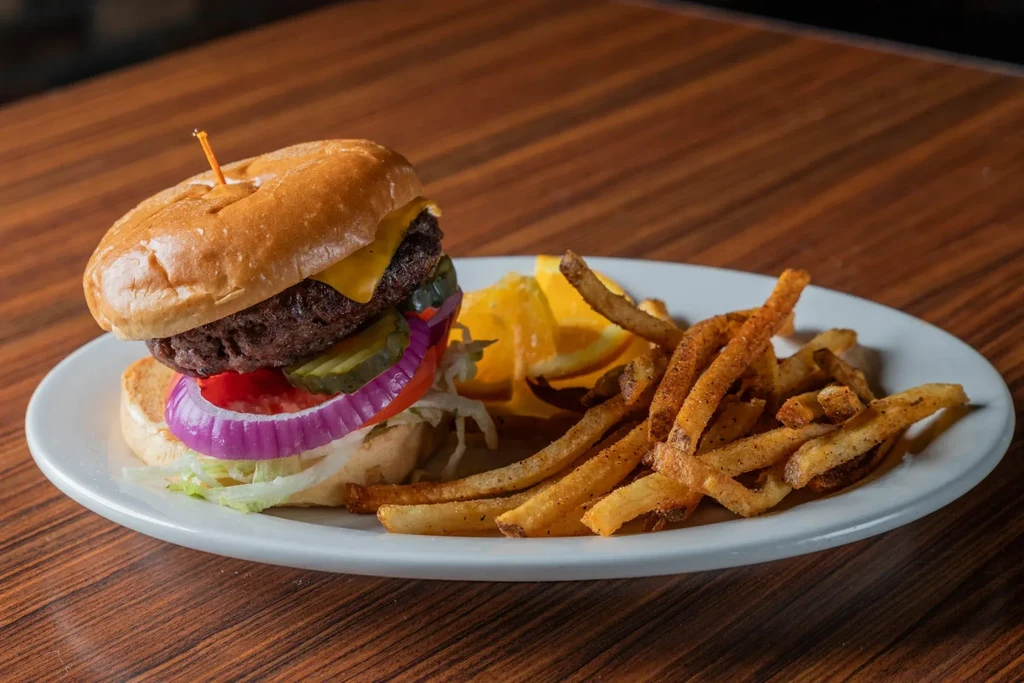 Cheeseburger, french fries, and orange slices on a white plate.