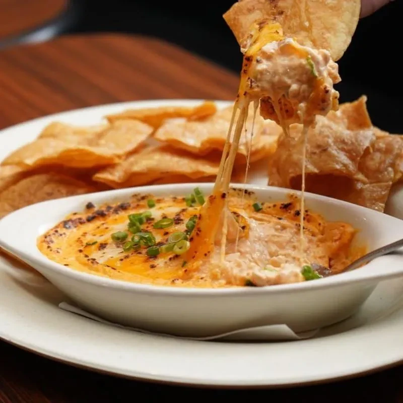 A chip pulls stretchy melted cheese from a golden, broiled dip.
