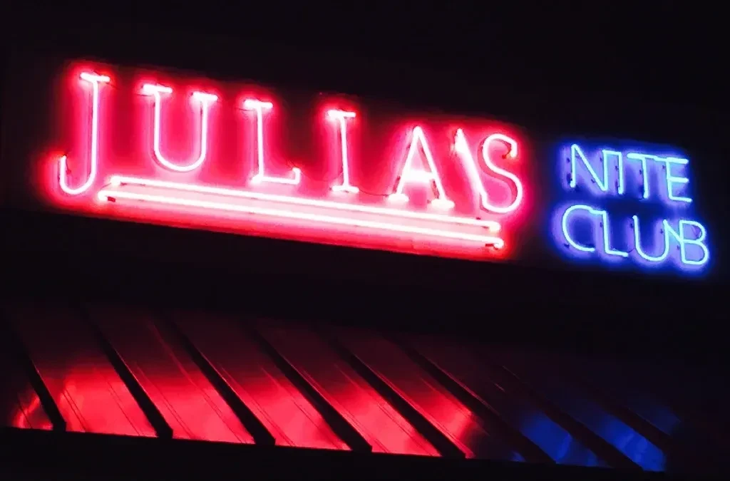 Red and blue neon sign for "JULIA'S NITE CLUB" at night.
