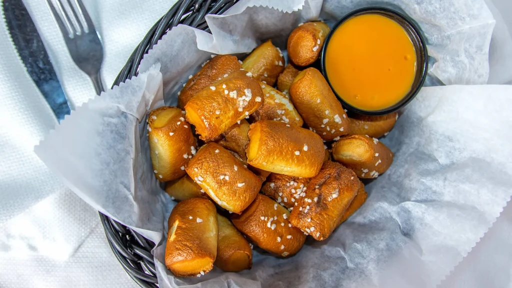 Overhead view of a basket of salted pretzel bites with cheese dip.