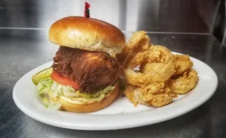 Crispy fried chicken sandwich with lettuce, tomato, pickle, and onion rings.