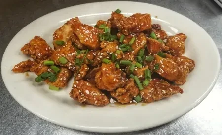 Fried chicken pieces with reddish-brown glaze, sesame, and green onions.