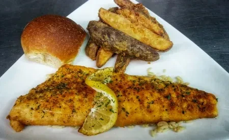 Plated meal with seasoned fish, potato wedges, rice, and a bread roll.