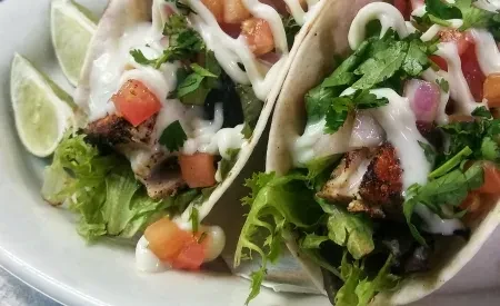 Two grilled protein tacos with fresh vegetables, creamy sauce, and lime.