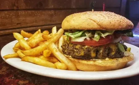 Cheeseburger with melted cheese and golden fries on white plate.