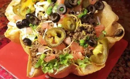 Crispy tortilla bowl filled with taco salad, meat, cheese, and vegetables.