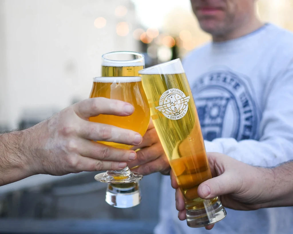 Hands clinking three beer glasses, one from Yellow Springs Brewery.