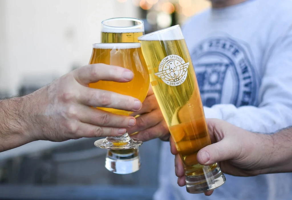 Three hands clinking different beer glasses, one from Yellow Springs Brewery.