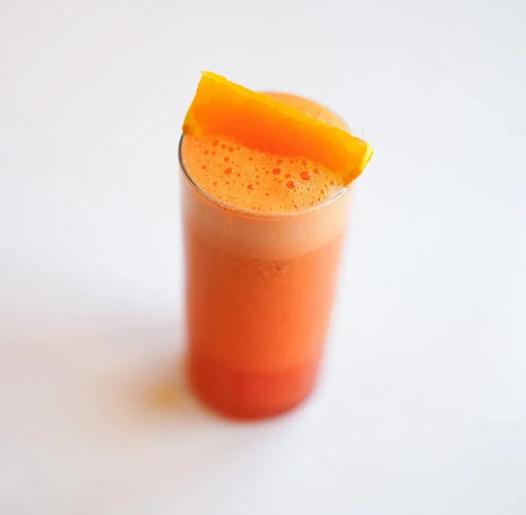 Tall glass of frothy orange drink with a fruit wedge.