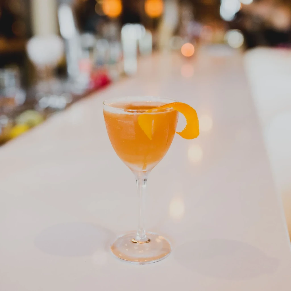 Cold amber cocktail with orange peel in coupe glass on bar.