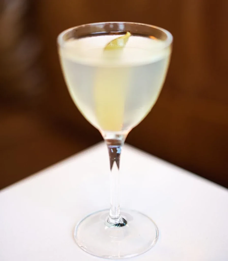 Clear, pale yellow cocktail in stemmed glass with curled citrus peel.