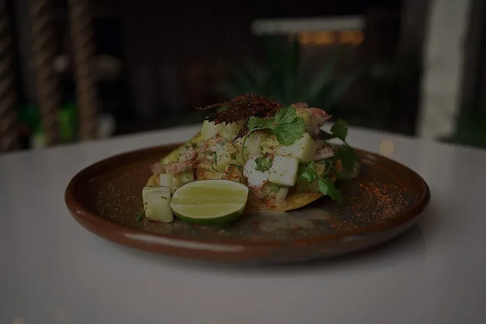 Seafood tostada with cheese, cilantro, chili, and lime on rustic plate.