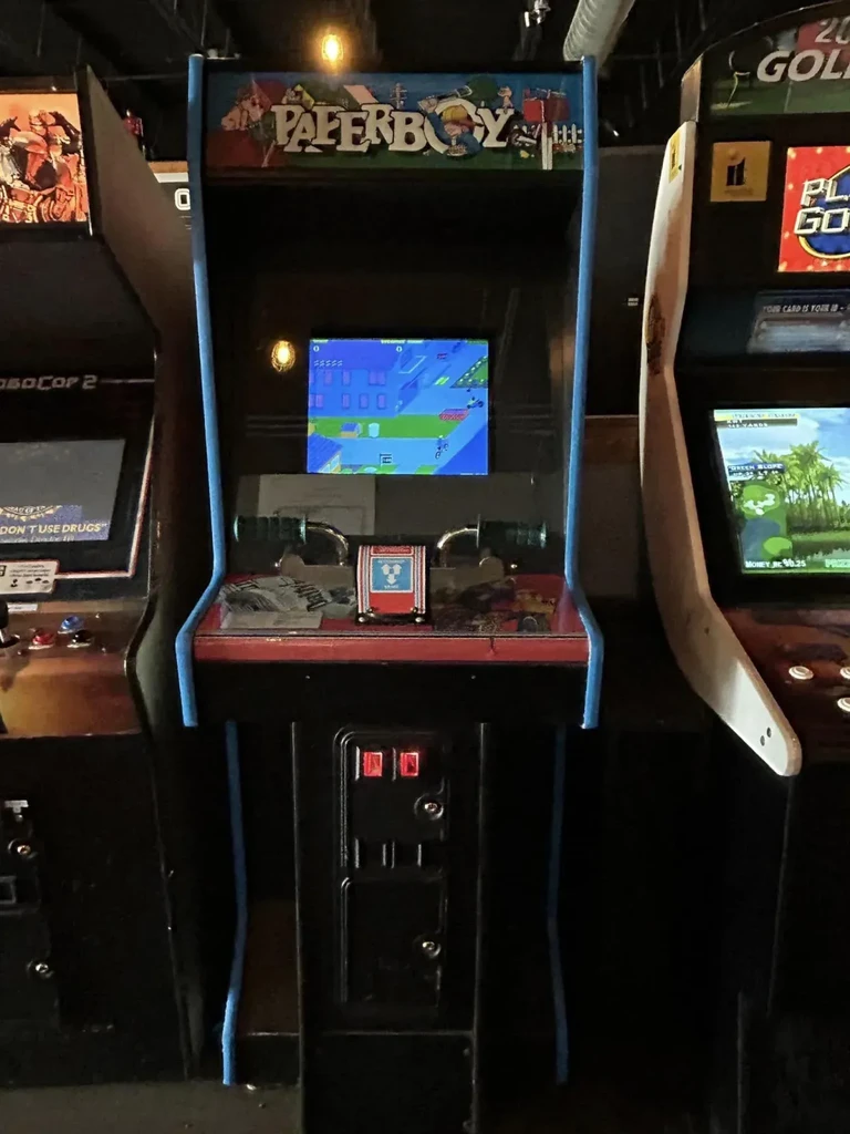 A Paperboy arcade game with other machines in a dimly lit room.